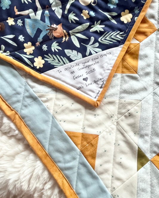 Quilt in soft blues with yellow accents featuring a handwritten quilt label attached to the corner of the quilt under the binding. 